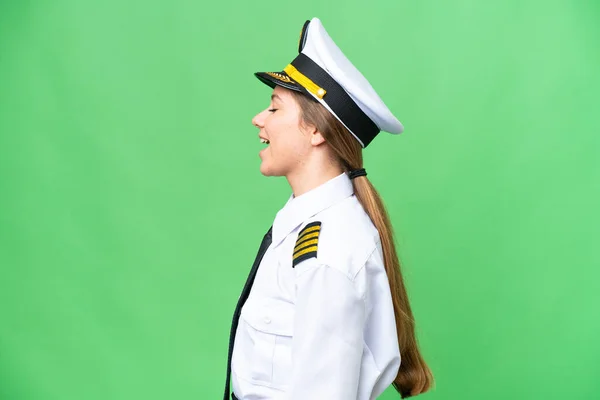 Airplane pilot woman over isolated chroma key background laughing in lateral position