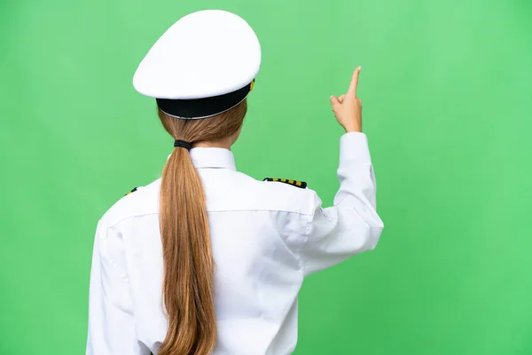 Airplane pilot woman over isolated chroma key background pointing back with the index finger