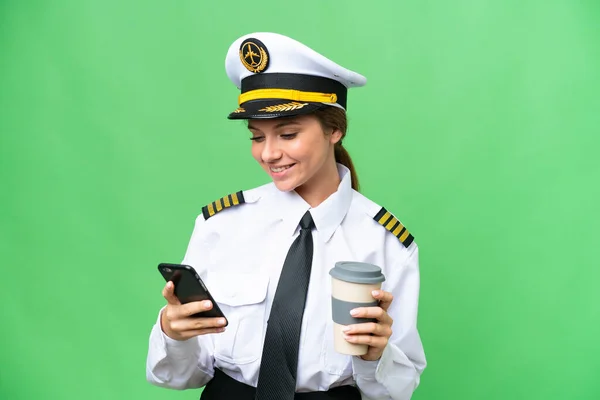 Airplane pilot woman over isolated chroma key background holding coffee to take away and a mobile