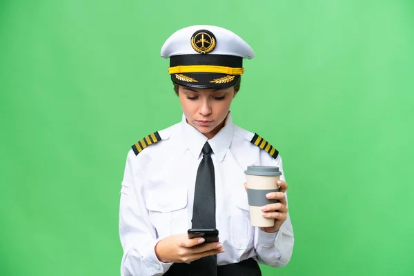 Stock image Airplane pilot woman over isolated chroma key background holding coffee to take away and a mobile