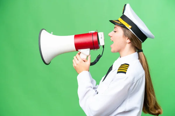 Airplane pilot woman over isolated chroma key background shouting through a megaphone