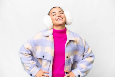 İzole edilmiş beyaz arka plan üzerinde kışlık manşetler takan genç bir kadın kolları kalçasında ve gülümsüyor.