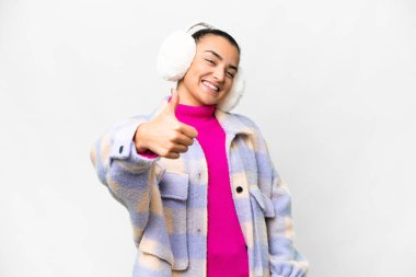 İzole edilmiş beyaz arka planda kışlık manşet takan genç bir kadın. Başparmakları havada çünkü iyi bir şey oldu.