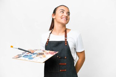 İzole edilmiş beyaz arka plan üzerinde palet tutan genç sanatçı kadın yukarı bakarken bir fikir düşünüyor.