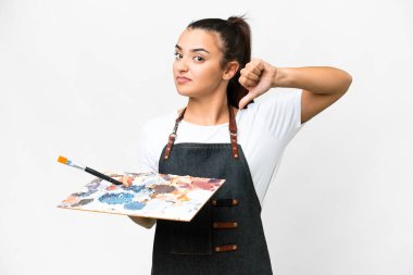 İzole edilmiş beyaz arkaplan üzerinde palet tutan genç bir sanatçı kadın negatif ifadeyle baş parmağını aşağı gösteriyor.