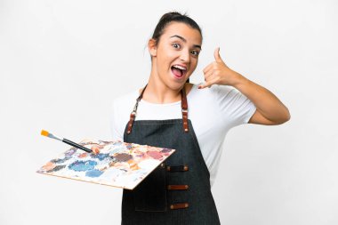 İzole edilmiş beyaz arka plan üzerinde palet tutan genç bir sanatçı telefon jesti yapıyor. Bana geri dönüş işareti ver.