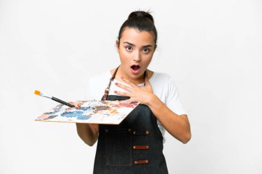 İzole edilmiş beyaz arka plan üzerinde palet tutan genç sanatçı kadın sağa bakarken şaşırdı ve şok oldu.