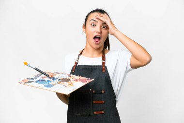 İzole edilmiş beyaz arka plan üzerinde palet tutan genç sanatçı kadın yan tarafa bakarken sürpriz jest yapıyor.