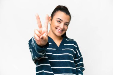 İzole edilmiş beyaz arka planda genç bir kadın gülümsüyor ve zafer işareti gösteriyor.