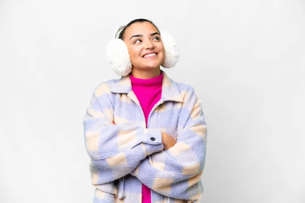 Young woman wearing winter muffs over isolated white background looking up while smiling