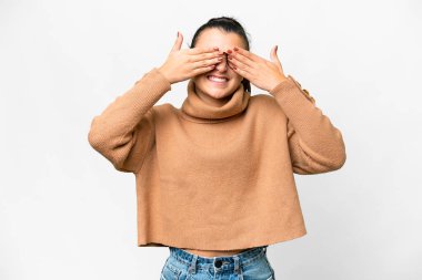 İzole edilmiş beyaz arka planda genç bir kadın. Gözleri elleriyle kaplıyor ve gülümsüyor.