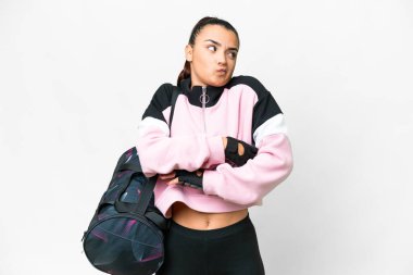 Young sport woman with sport bag over isolated white background making doubts gesture while lifting the shoulders