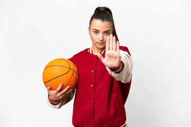 İzole edilmiş beyaz arka planda basketbol oynayan genç bir kadın dur hareketi yapıyor.