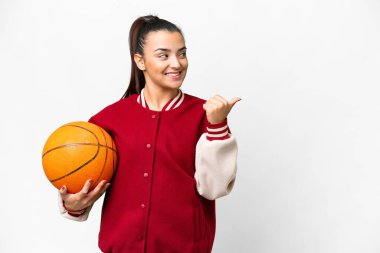 İzole edilmiş beyaz arka planda basketbol oynayan genç bir kadın bir ürünü sunmak için kenarı işaret ediyor.