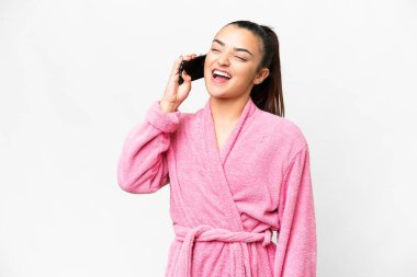 İzole edilmiş beyaz arka planda bornozlu genç bir kadın cep telefonuyla sohbet ediyor.