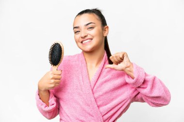 Bornozlu genç kadın saçlarını tarayıp soyutlanmış beyaz arka planda gururlu ve kendini beğenmiş.