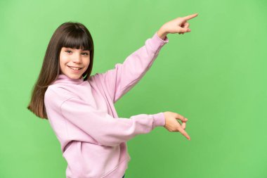 Küçük kız izole edilmiş yeşil krom anahtar arka planda parmak göstererek bir ürün sunuyor.