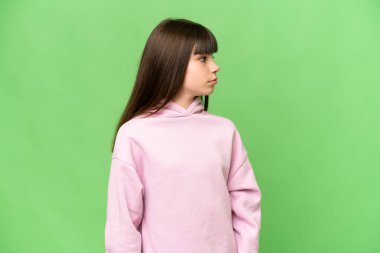 İzole edilmiş yeşil krom anahtar arka planı olan küçük kız yan tarafa bakıyor.