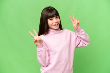 Yeşil renkli arka planda küçük bir kız zafer işaretini iki eliyle gösteriyor.