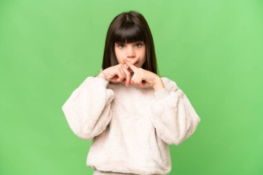 İzole edilmiş yeşil renkli arka plan üzerinde küçük bir kız sessizlik işareti gösteriyor.