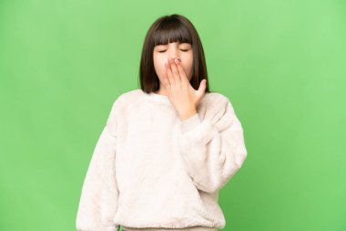 Küçük kız izole edilmiş yeşil krom anahtar arka planda esniyor ve geniş ağzını eliyle kapatıyor.