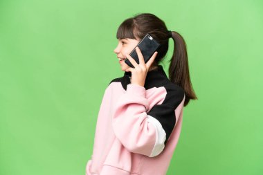 İzole edilmiş yeşil renkli anahtar geçmişi olan küçük bir kız cep telefonuyla sohbet ediyor.