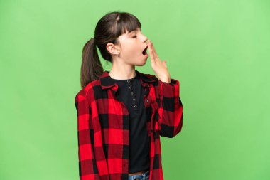 Küçük kız izole edilmiş yeşil krom anahtar arka planda esniyor ve geniş ağzını eliyle kapatıyor.