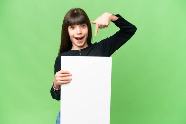 Küçük kız izole edilmiş krom anahtar arka planda elinde mutlu bir ifadeyle boş bir levha tutuyor ve ona doğrultuyor.