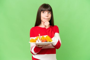 İzole edilmiş krom arka planda waffle tutan küçük bir kız şüpheleri ve düşünceleri var.