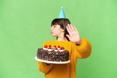 Küçük kız, elinde doğum günü pastası tutarken izole edilmiş krom anahtar arkaplanını durduruyor ve hayal kırıklığına uğruyor.