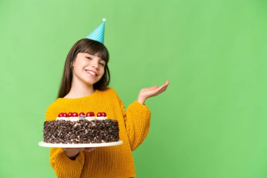 Doğum günü pastası tutan küçük kız izole edilmiş krom anahtar arka planda. Davet etmek için ellerini yana uzatıyor.