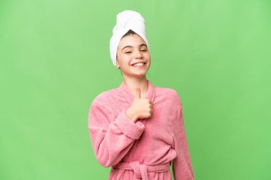 İzole edilmiş krom anahtar geçmişi olan bornozlu küçük bir kız baş parmak hareketi yapıyor.