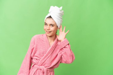 İzole edilmiş krom arka planda bornozlu küçük bir kız kulağına elini sürerek bir şeyler dinliyor.