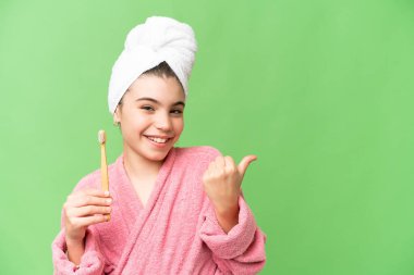 İzole edilmiş krom arka planda dişlerini fırçalayan küçük kız bir ürünü sunmak için yan tarafı işaret ediyor.