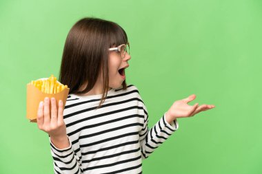 Küçük kız izole edilmiş krom anahtar zemin üzerinde kızarmış çipler tutuyor ve sürpriz yüz ifadesi var.