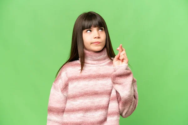 Little girl over isolated green chroma key background with fingers crossing and wishing the best