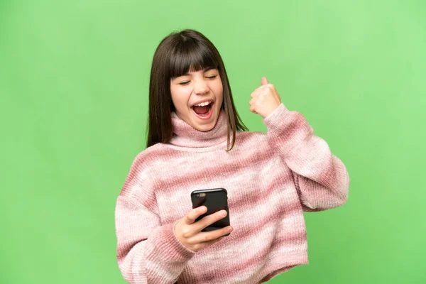 stock image Little girl over isolated green chroma key background with phone in victory position