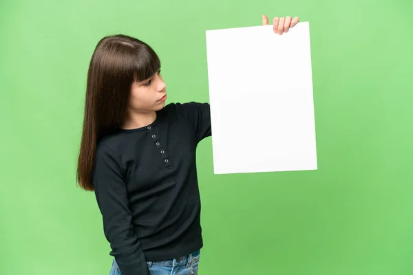 小女孩拿着一个空的标语牌 站在孤立的彩色背景上看着它 — 图库照片