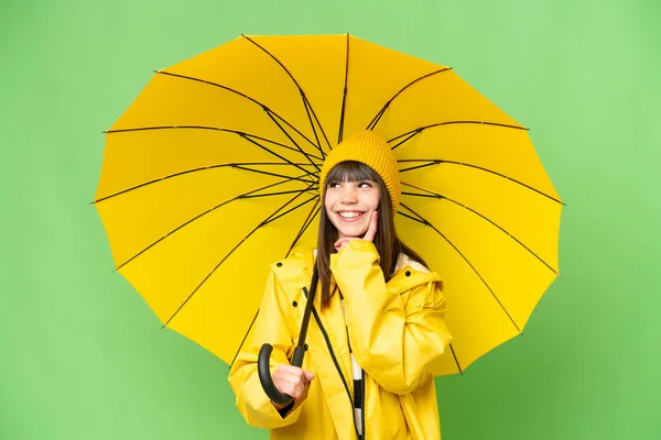 女の子ともにレインプルーフコートと傘上の隔離されたクロマキー背景考えますAアイデアながら見上げます — ストック写真