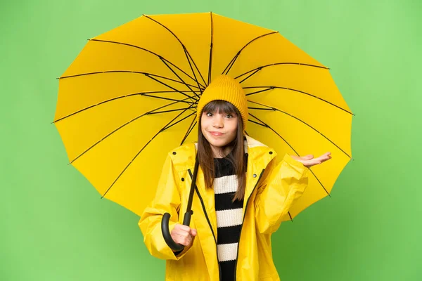 小さな女の子とともにレインプルーフコートと傘上の隔離されたクロマキーバック持っています疑問ながら手を上げます — ストック写真