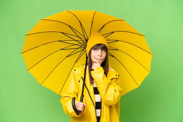 小さな女の子ともにレインプルーフコートと傘上の隔離されたクロマキー背景持っている疑問と思考 — ストック写真