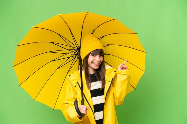 小さな女の子とともにレインプルーフコートと傘上の隔離されたクロマキー背景指差し指で側面 — ストック写真