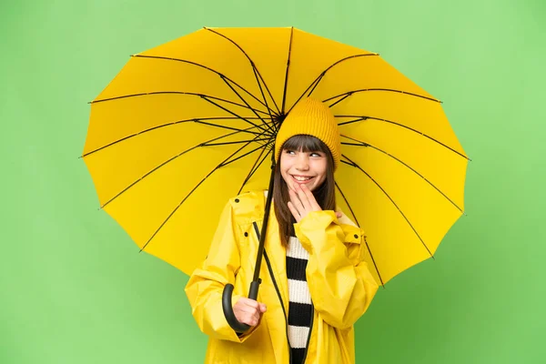 小さな女の子とともにレインプルーフコートと傘上の隔離されたクロマキー背景上を見上げます上の笑顔 — ストック写真