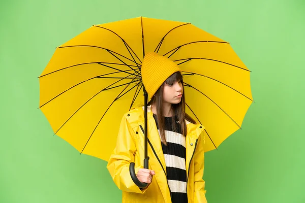 小さな女の子とともにレインプルーフコートと傘上の隔離されたクロマキー背景見ますザサイド — ストック写真