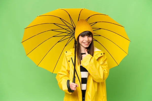 女の子ともにレインプルーフコートと傘上の隔離されたクロマキーバック与えますザ親指アップジェスチャー — ストック写真