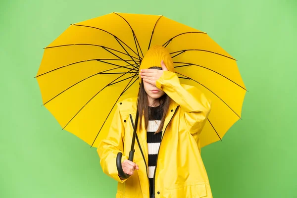手で目をカバー隔離されたクロマキーの背景にレインプルーフコートと傘を持つ少女 何か見たくない — ストック写真