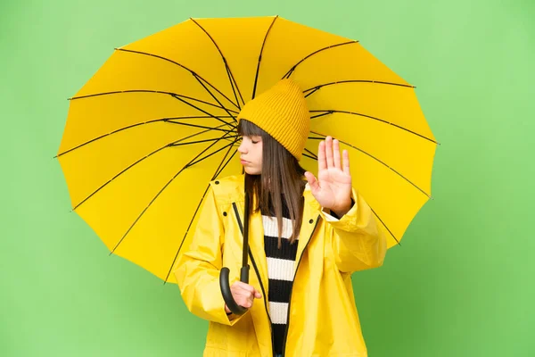 小さな女の子とともにレインプルーフコートと傘上の隔離されたクロマキー背景作りストップジェスチャーと失望 — ストック写真