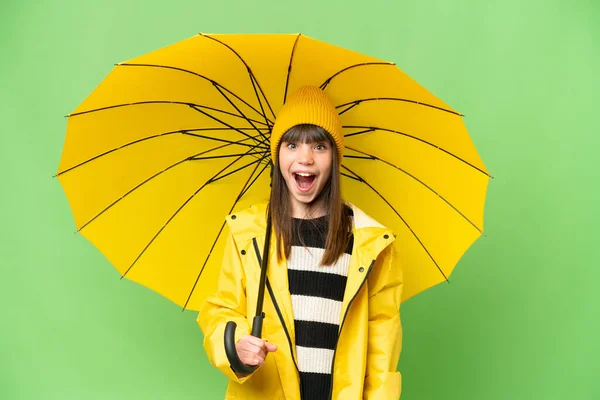 小さな女の子とともにレインプルーフコートと傘上の隔離されたクロマキー背景とともに驚きの顔の表情 — ストック写真