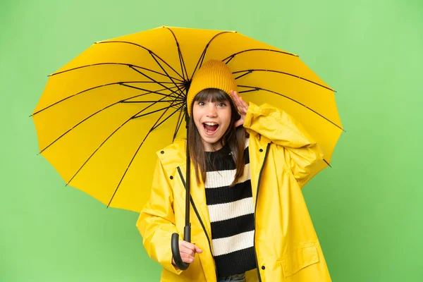 小さな女の子とともにレインプルーフコートと傘上の隔離されたクロマキー背景とともに驚きの表情 — ストック写真