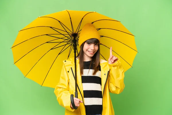 小さな女の子とともにレインプルーフコートと傘上の隔離されたクロマキー背景ショーと持ち上げる指でベストの印 — ストック写真